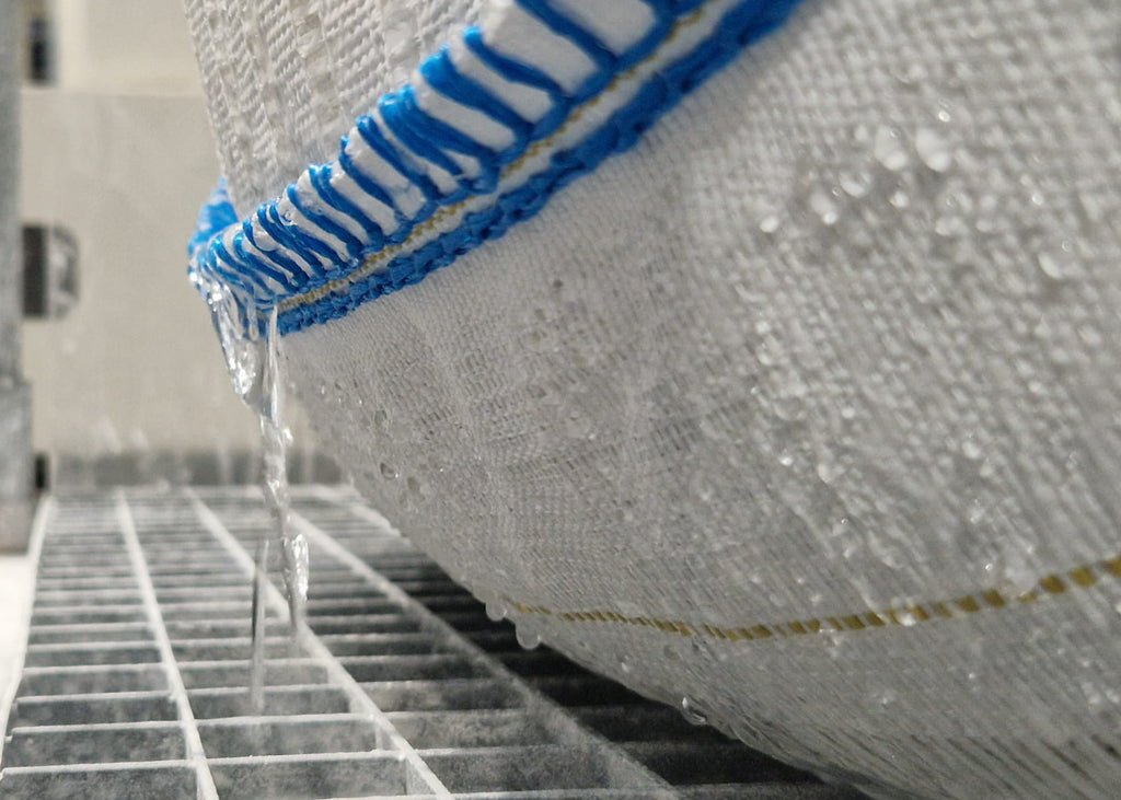 photo showing clean, treated industrial water flowing from an Aspifloc filter bag which has held the paint solids ready for disposal